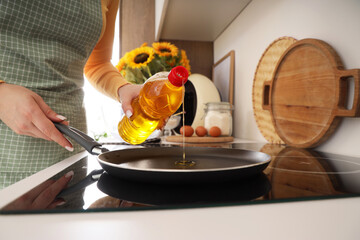 Woman pouring sunflower oil into frying pan in kitchen, closeup