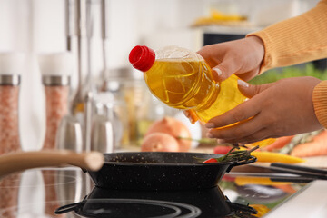 Female hands pouring sunflower oil into frying pan in kitchen, closeup