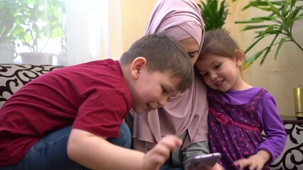 Online communication and congratulations on the Eid holiday. A happy Muslim family, a woman in a hijab with her young son and daughter, greet their relatives and friends remotely