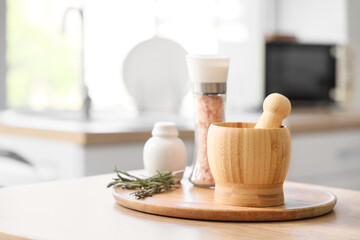 Wooden mortar with pestle and rosemary on table in kitchen, closeup