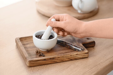 Female hand grinding peppercorns in mortar on table, closeup