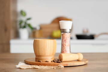 Wooden mortar with pestle, peppercorns and sea salt on table in kitchen, closeup