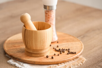 Wooden mortar with pestle, peppercorns and sea salt on table in kitchen, closeup