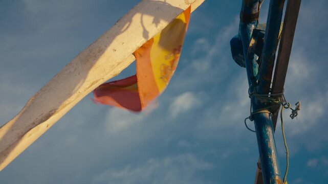 A weathered Spanish flag gently flutters from an old fishing boat in warm sunset light. Symbolic, textured and coastal scene.