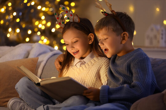 Cute little children reading Christmas story on sofa at home in evening