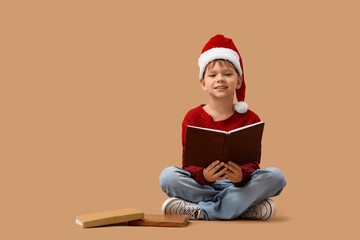 Naklejka premium Cute little boy in Santa hat reading Christmas story on beige background
