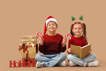 Naklejka premium Cute little children with book and Christmas gifts sitting on beige background