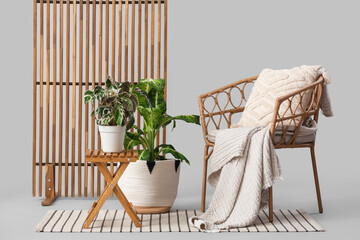 Armchair with wooden table, plants and folding screen on light background