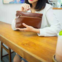A girl's body in a gray skirt and white shirt sits in a cafe and holds an elegant tan leather handbag.