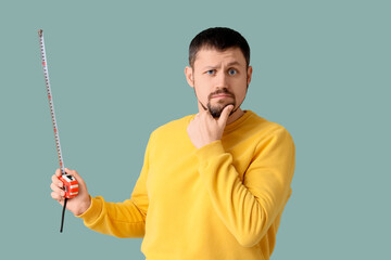 Thoughtful young man with tape measure on green background