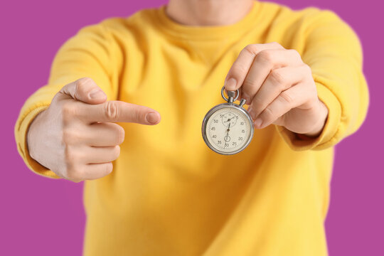 Young man pointing at stopwatch on violet background, closeup
