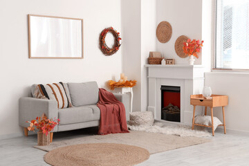 Fototapeta premium Comfortable sofa, fireplace and vases with beautiful autumn leaves in interior of living room