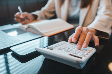 Close-up of a business professional using a calculator and notebook for financial planning in a modern office environment.
