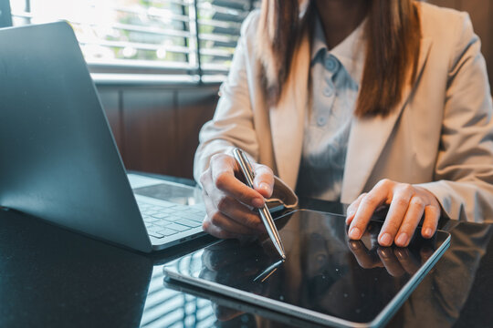 Professional woman working on a digital tablet and laptop in a modern office environment.