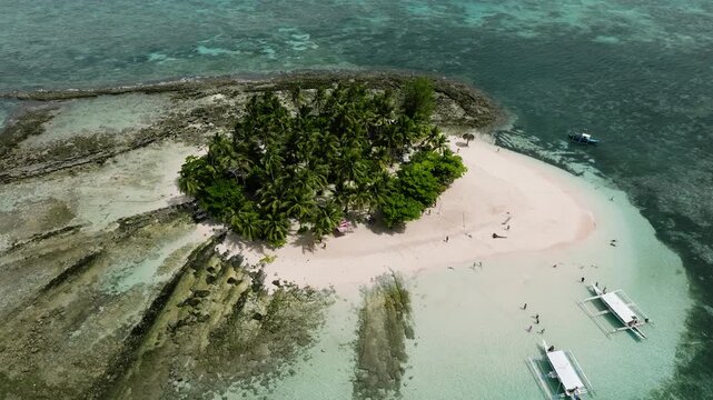 Small tropical island with palm trees, white sand beach, clear turquoise water and boats nearby. Guyam Island. Siargao, Philippines.