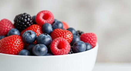 White bowl full of fresh mixed berries including strawberries raspberries and blackberries close up