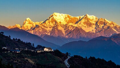 "Golden-lit snow-covered mountain peak with forested ridges under clear gradient sky"