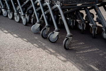 Close-up row of metal shopping cart caster wheels parked on an asphalt surface outside a supermarket.