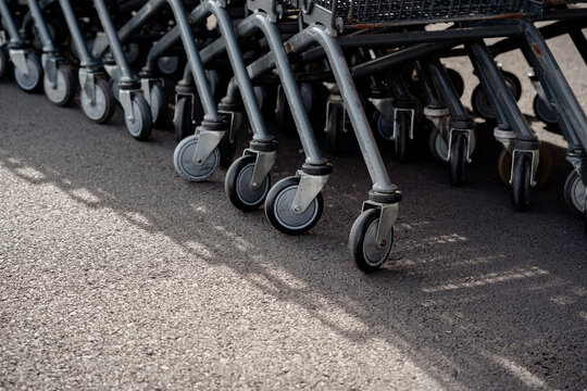Close-up row of metal shopping cart caster wheels parked on an asphalt surface outside a supermarket.