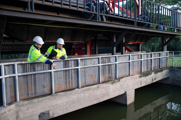 Naklejka premium A professional engineer and an inspector are jointly seriously inspecting the water filtration of a water filter inside a treatment pond.