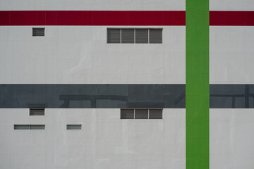 Modern building exterior wall facade with geometric red, green, and grey painted stripes and vents.