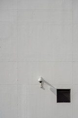 Security dome CCTV camera mounted on a minimalist gray tiled wall next to a small black vent.