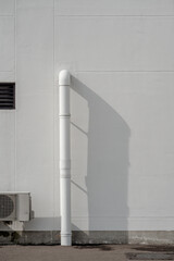 White drain pipe and air conditioner outdoor unit on a textured wall with strong geometric shadows.