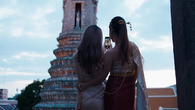 Thai women in traditional dress taking selfie with temple background