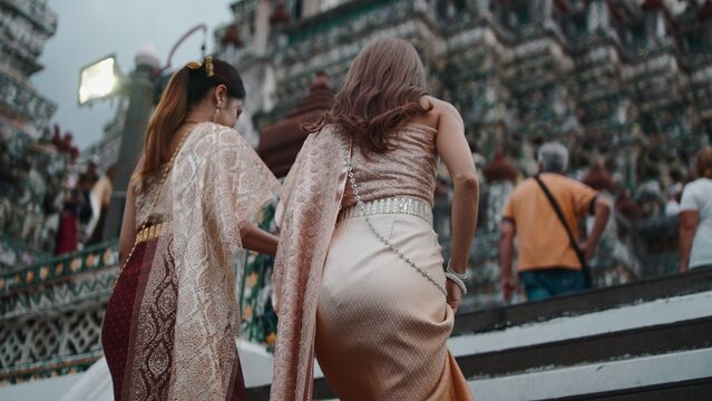 Thai women in traditional chut thai walking up temple steps, celebrating culture