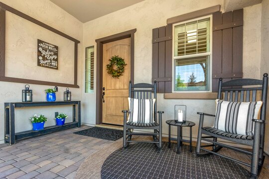 A welcoming porch featuring chairs and a stylish black door in a lovely house - Powered by Adobe