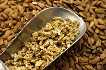 Walnut kernels in metal scoop with almond background showing mixed nuts texture closeup