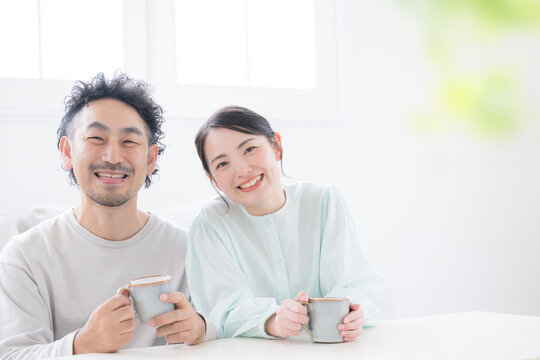 A relaxed scene of a smiling couple holding coffee cups and leaning close together, looking directly at the camera.