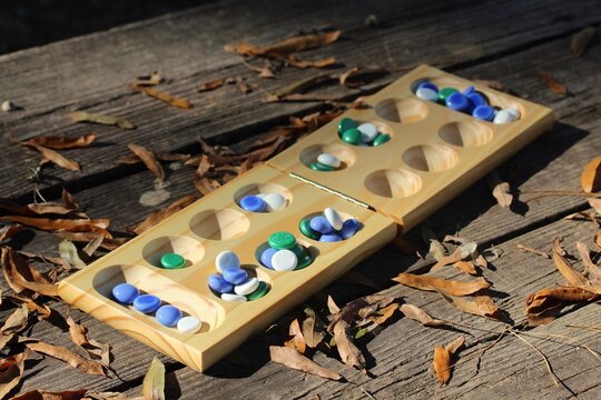 Mancala game in the outdoors on a wooden table among autumn leaves and sunlight