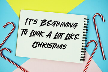 It's Beginning To Look A Lot Like Christmas message of season holidays written on notepad with candy cane decoration on pastel background