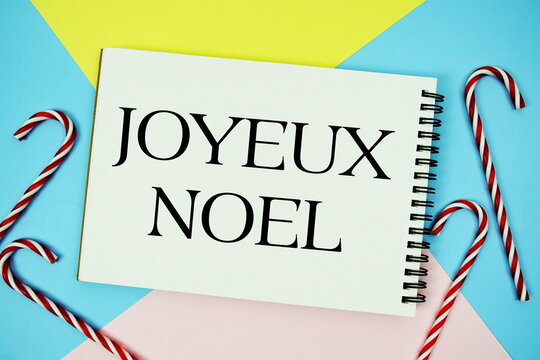 Joyeux Noel message of season holidays written on notepad with candy cane decoration on pastel background
