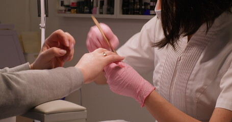 Modern manicure. Gel polish. Beauty technician nail hands in pink gloves using emery board on fingernails care female routine cosmetic treatment.