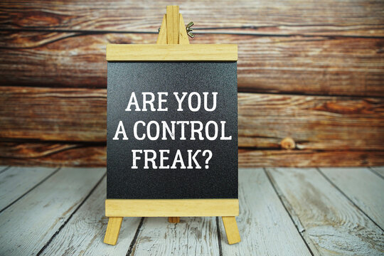 wooden easel holds a blackboard with the white text "Are You a Control Freak?" set against a rustic wooden wall and light-colored wooden floor