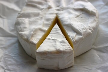 A camembert wheel with a triangular slice pulled out shows its creamy interior and textured rind. Clean culinary image for recipes, ads and menus.
