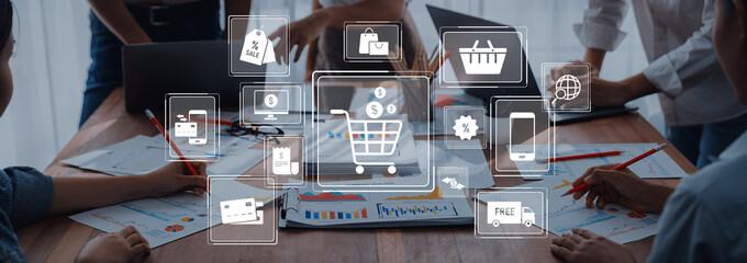 A team discusses digital marketing strategies in an office setting, surrounded by laptops and charts, with shopping cart icons highlighting ecommerce concepts. Trope