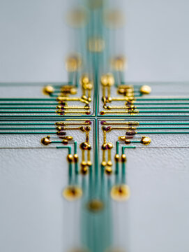 Detailed macro view of an intricate green and gold electronic circuit board showcasing precise soldered connections and thin parallel conductive lines on a white sur