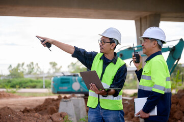 Civil engineers coordinate construction work with laptop and radio at infrastructure site. Supervise new road construction, inspect project, construction teamwork in Thailand Asia.