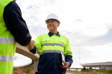 Construction engineers shaking hands at road construction site, showing teamwork, agreement, cooperation, and professional collaboration in civil engineering work.