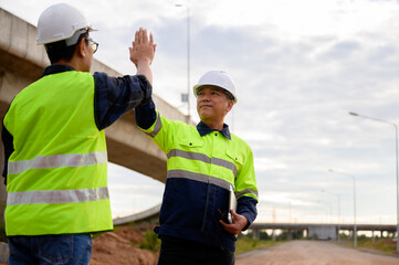 Construction engineers celebrating teamwork with a high five at road construction site, symbolizing cooperation, success, and positive collaboration.