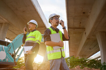 Construction engineers communicate with radios at road construction site. Inspect structure, supervise new infrastructure work, civil engineer outdoor at Thailand Asia construction site.