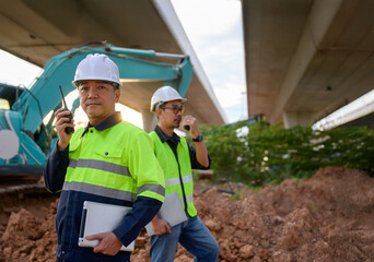 Construction engineers communicating with walkie talkies while supervising road construction work, ensuring coordination and field inspection at infrastructure site.