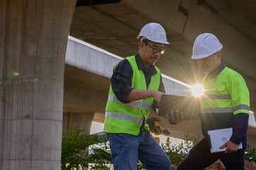 Civil engineers reviewing construction plans on laptop at infrastructure site, supervising road construction and coordinating field operations.