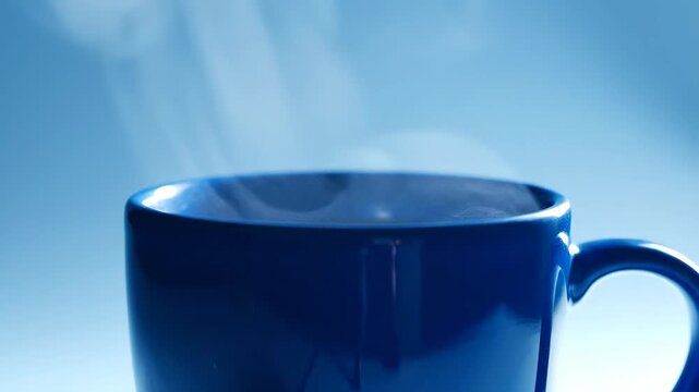 A blue mug steams against a blurred blue background The steam rises from the cups rim
