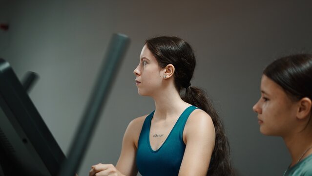 Young woman exercising on an elliptical machine, training at fitness gym - Powered by Adobe
