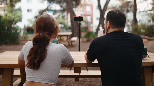 People recording outdoor content, sitting at picnic table with smartphone on tripod
