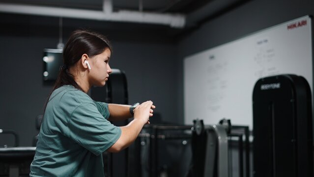 Young woman exercising squats in gym, monitoring fitness progress on smartwatch - Powered by Adobe